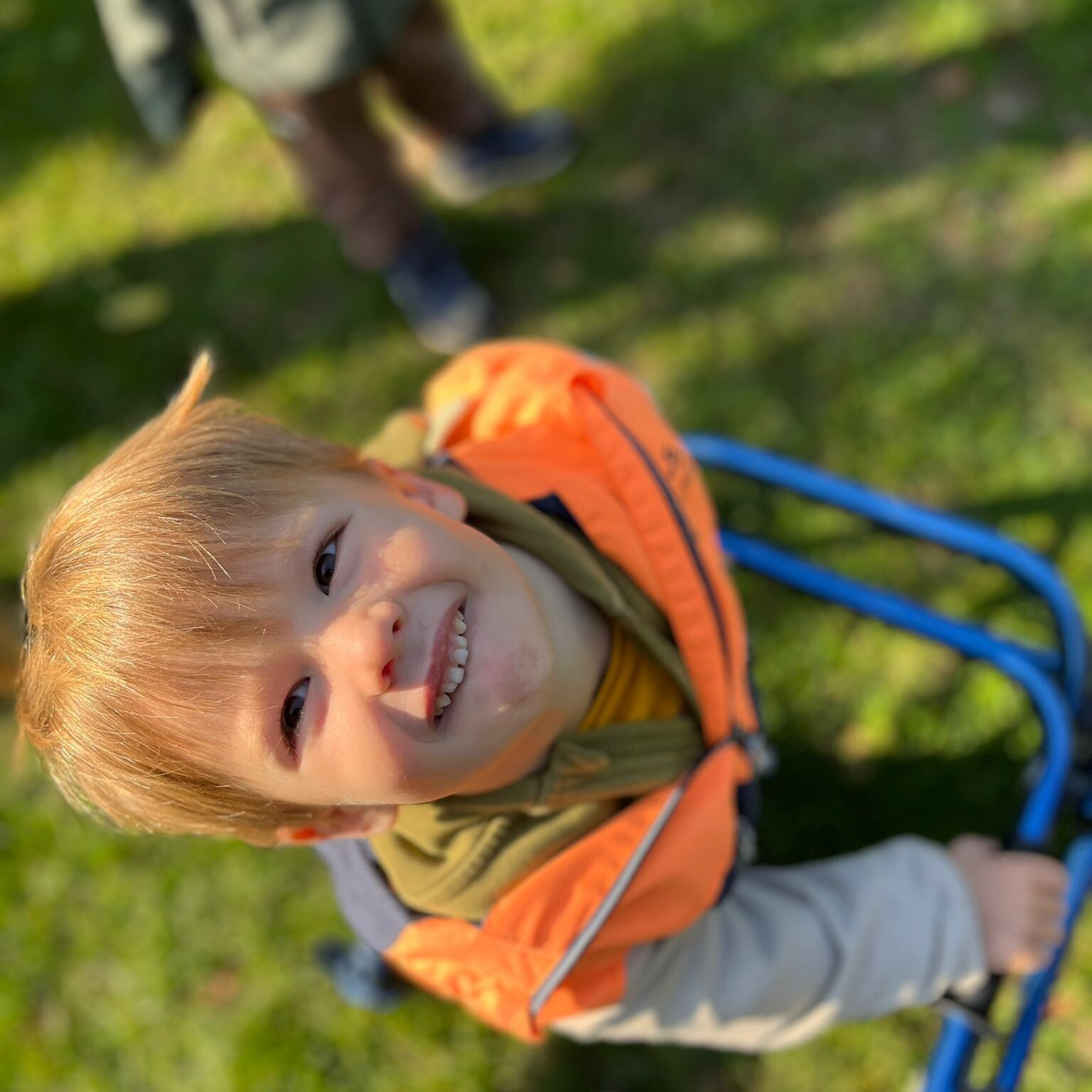 Kleine jongen met loophulpmiddel kijkt naar boven in de lens van de camera. Hij staat in het gras.